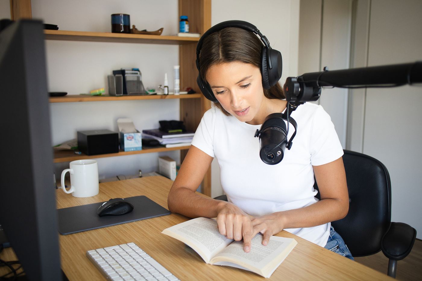 An author in headphones reading her book aloud into a microphone at a home desk