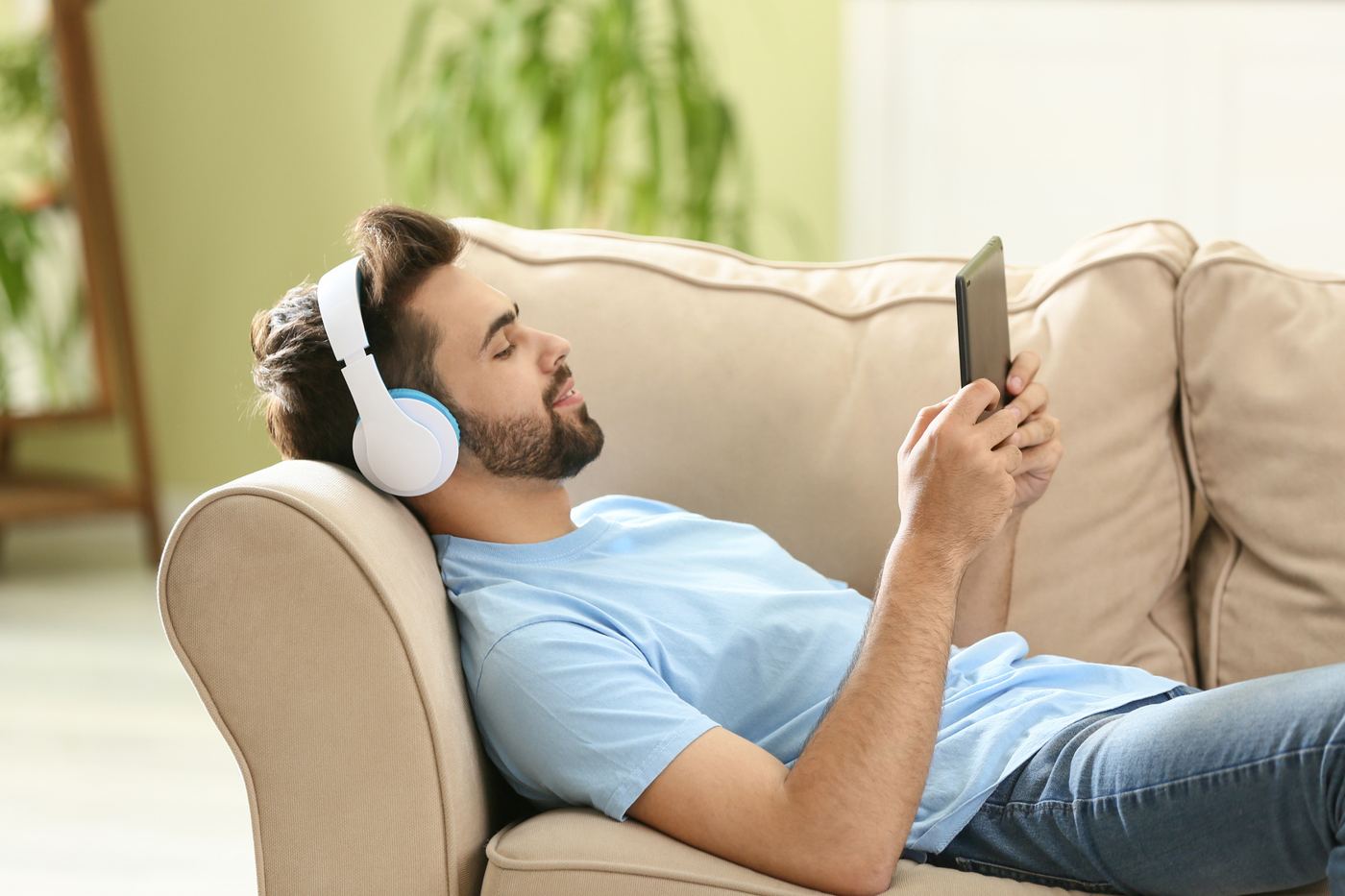 A man in headphones listening to an audiobook on a sofa