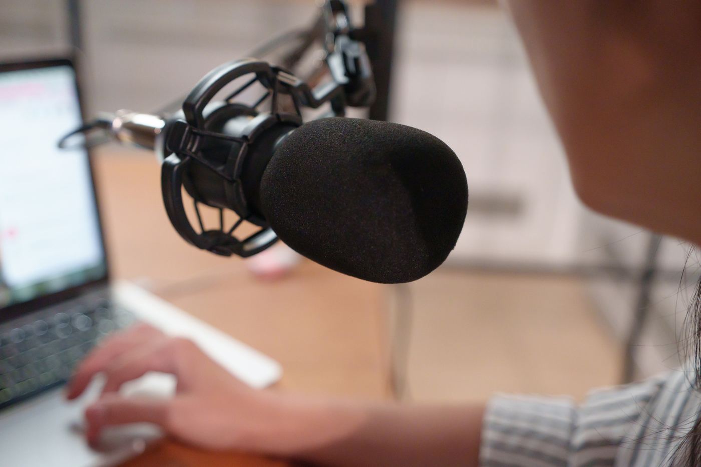 A microphone on a boom arm beside a laptop at a recording desk