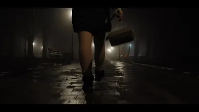 A woman walking through a foggy park at night, seen from behind